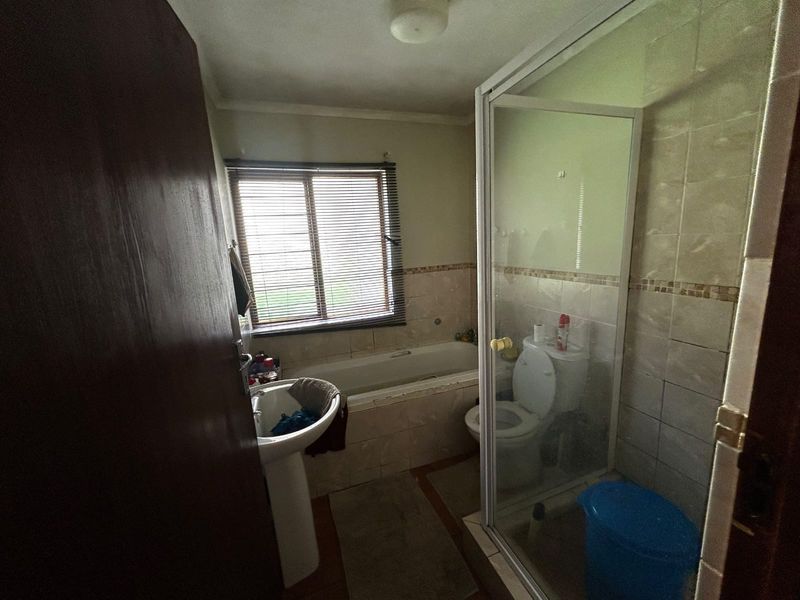A functional bathroom featuring a pedestal basin, built-in bathtub, separate shower enclosure, and toilet, with tiled finishes throughout.