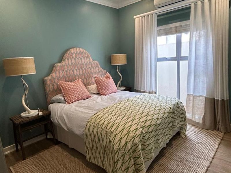A well-maintained bedroom featuring laminate flooring, recessed downlighting, and a wall-mounted split-system air conditioning unit.