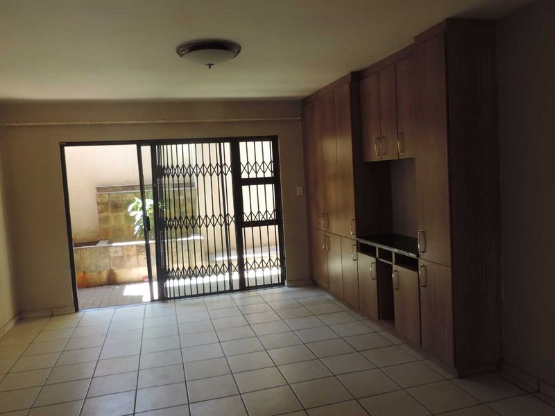 Spacious living area featuring tiled flooring, extensive built-in cabinetry, and direct access to a private outdoor patio through a secure sliding gate.