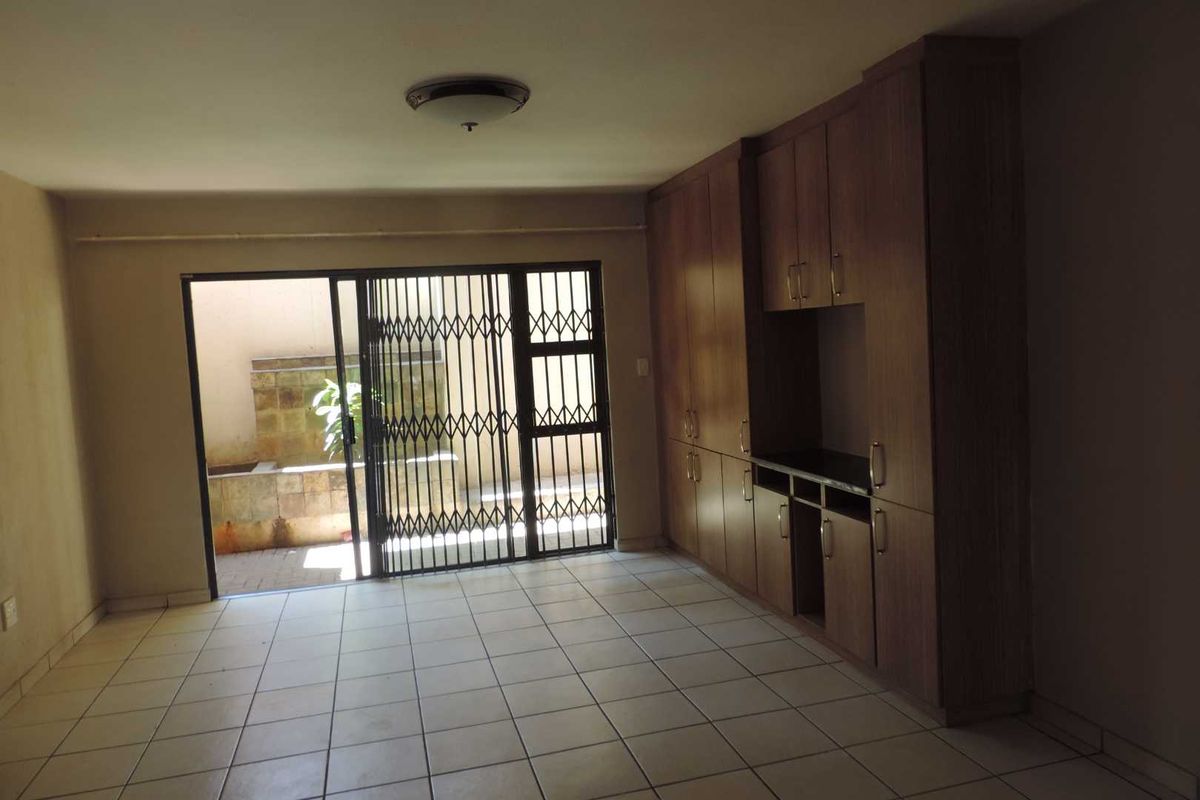 Spacious living area featuring tiled flooring, extensive built-in cabinetry, and direct access to a private outdoor patio through a secure sliding gate.