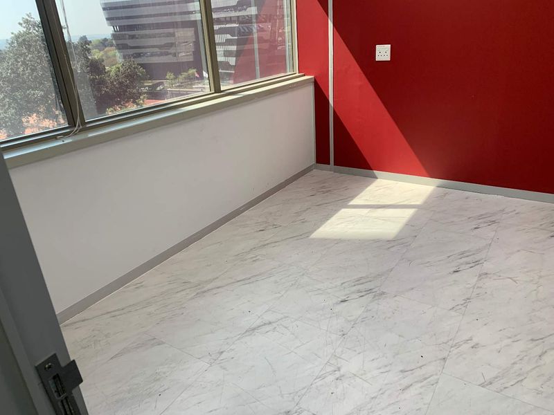 An empty office space featuring large windows, marble-effect vinyl flooring, and a bold red accent wall.