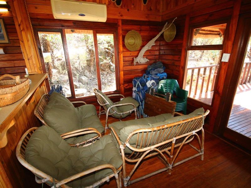A rustic living area featuring warm timber wall cladding, polished timber flooring, and large sliding doors that open onto an outdoor timber deck.