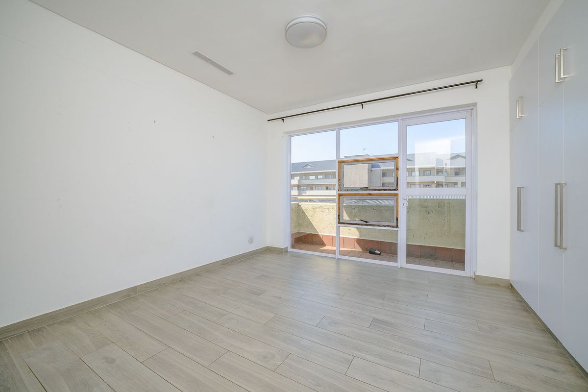 An empty bedroom featuring light-toned laminate flooring, built-in cupboards, and a sliding glass door providing access to a small balcony.