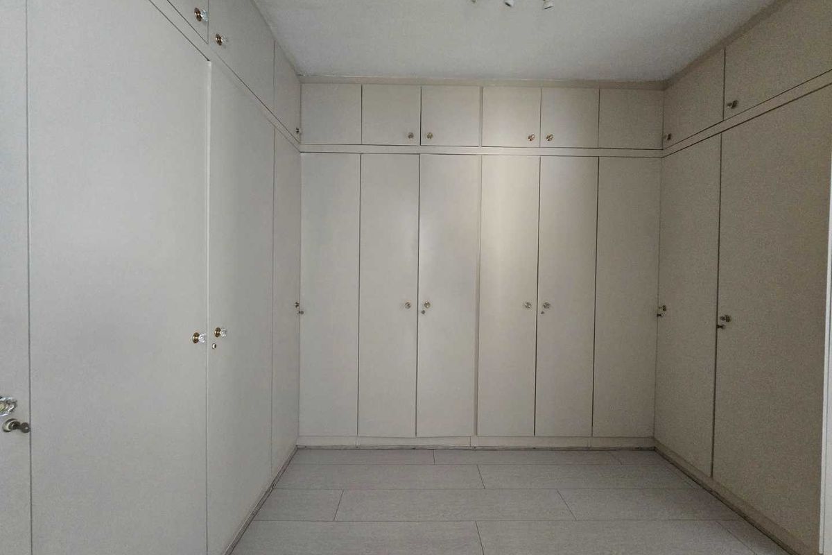 A spacious bedroom featuring extensive floor-to-ceiling built-in cupboards and neutral tiled flooring, offering a clean and functional storage-focused layout.