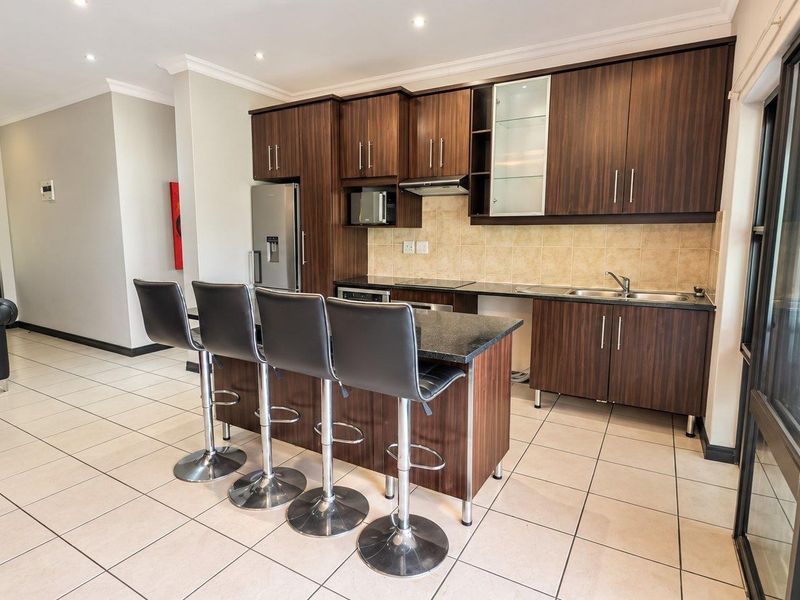 Modern open-plan kitchen featuring dark wood cabinetry, granite countertops, a central island, and tiled flooring, seamlessly integrated with the living area.
