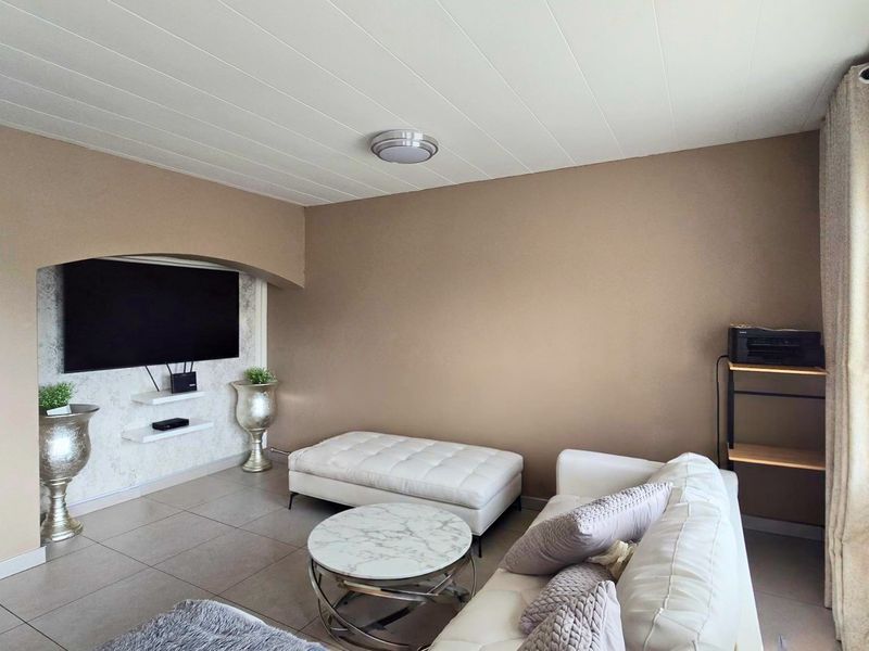 A comfortable living room featuring tiled flooring, a distinctive arched wall niche for media, and a clean tongue and groove ceiling finish.