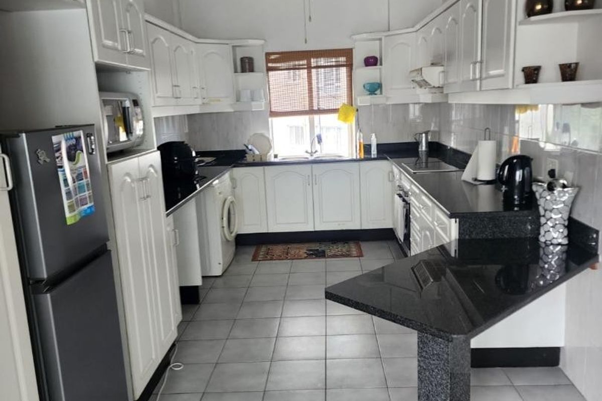 A functional kitchen featuring white cabinetry, black granite countertops, a breakfast bar, tiled flooring, and a ceiling fan.
