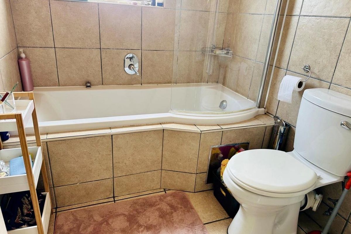 A functional bathroom featuring a tiled bathtub with a glass shower screen and a standard white toilet.