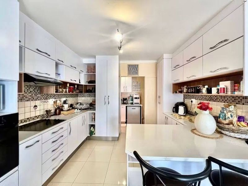Modern kitchen featuring white cabinetry, stone countertops, integrated appliances, and a tiled backsplash, offering a clean and functional workspace.
