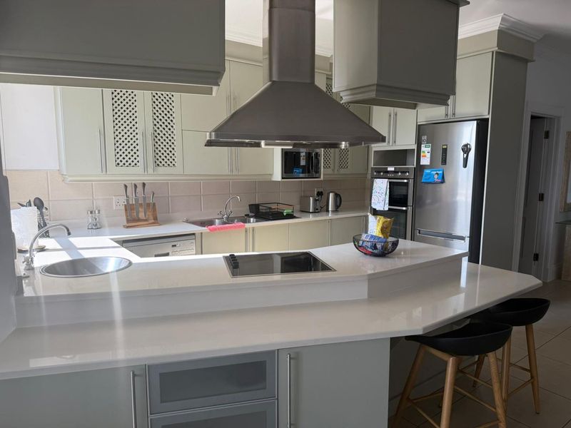 Modern kitchen featuring light-toned cabinetry, quartz countertops, a breakfast bar, and integrated stainless steel appliances including an oven and extractor fan.