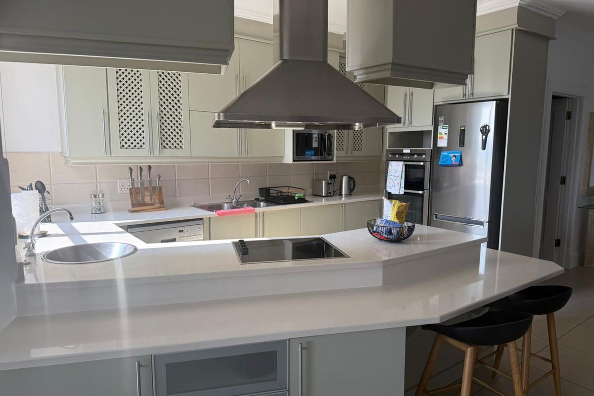 Modern kitchen featuring light-toned cabinetry, quartz countertops, a breakfast bar, and integrated stainless steel appliances including an oven and extractor fan.