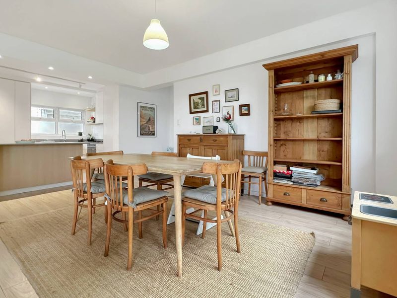 A bright open-plan dining and kitchen area featuring light laminate flooring, modern cabinetry, and a functional kitchen island with integrated appliances.