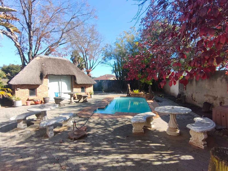 Outdoor pool area featuring a swimming pool, brick-paved patio, and a detached thatched-roof outbuilding set within a private garden space.