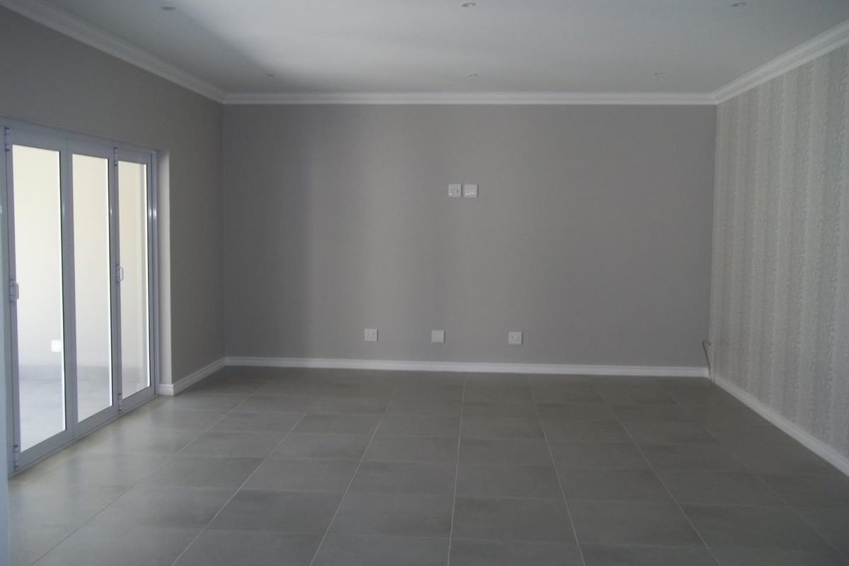 A spacious, empty living room featuring neutral grey tiled flooring, recessed ceiling lighting, and large glass sliding doors leading to an outdoor area.