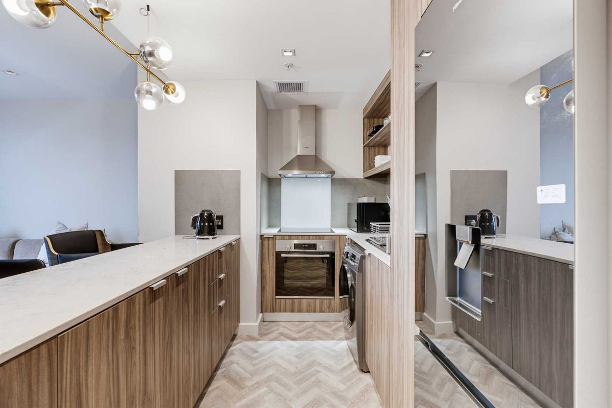 Modern galley-style kitchen featuring wood-grain cabinetry, stone countertops, herringbone flooring, and high-quality built-in appliances.