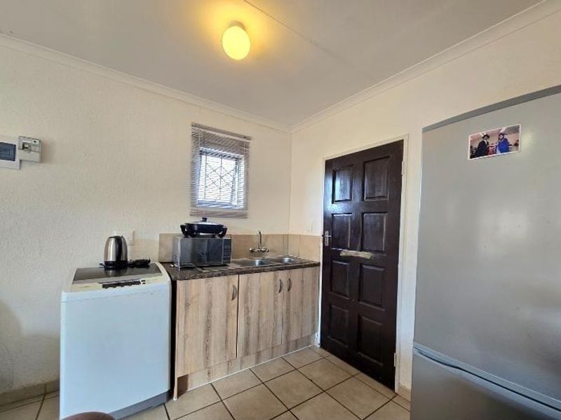 A functional laundry area featuring built-in cabinetry, a stainless steel sink, tiled flooring, and direct access through a secure door.