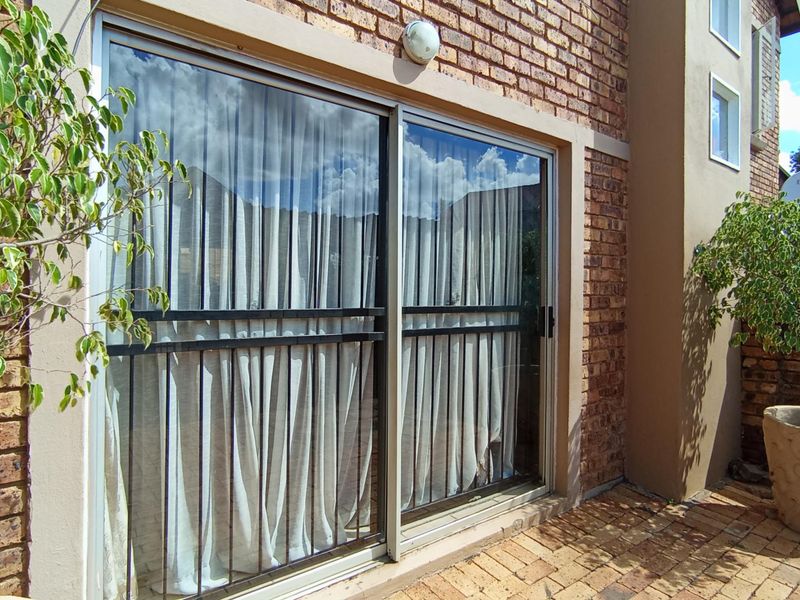 Rear exterior view of the townhouse featuring a paved patio area, exposed brickwork, and a sliding glass door with a security gate.