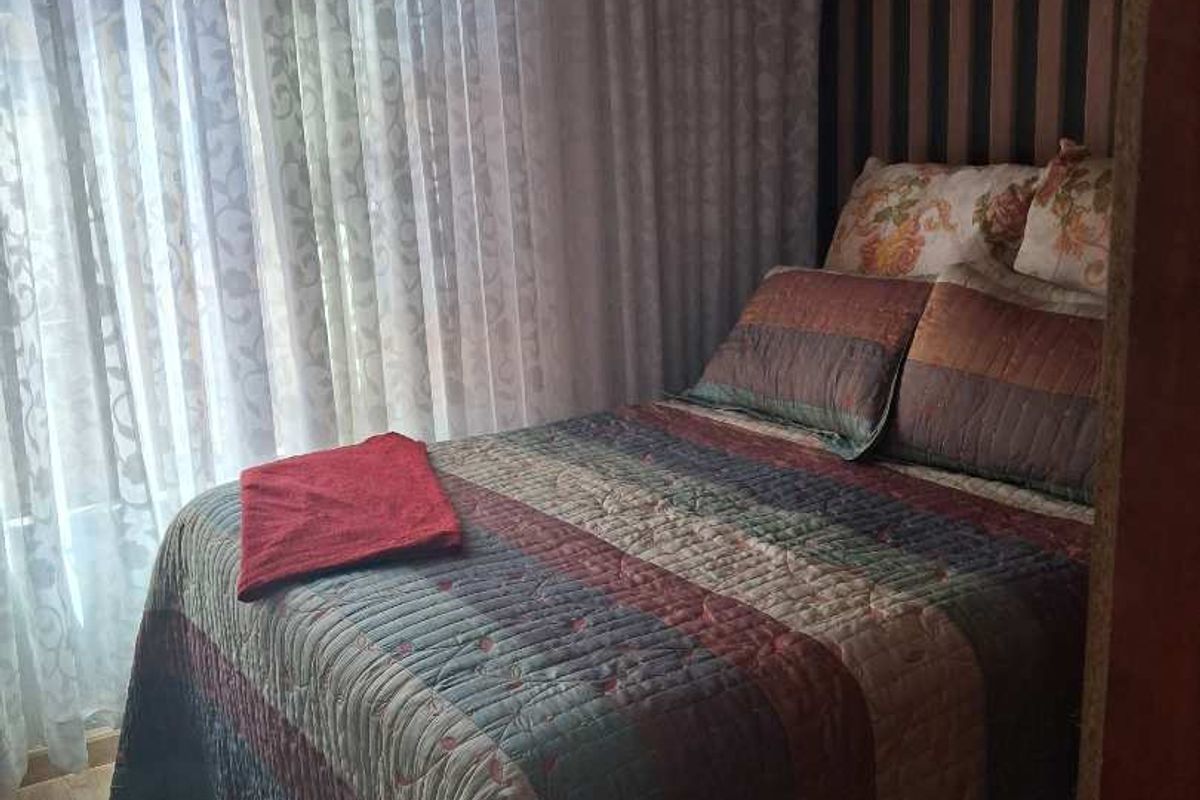 A cozy bedroom featuring wood-look flooring, vertical striped accent wallpaper, and floor-to-ceiling sheer curtains.