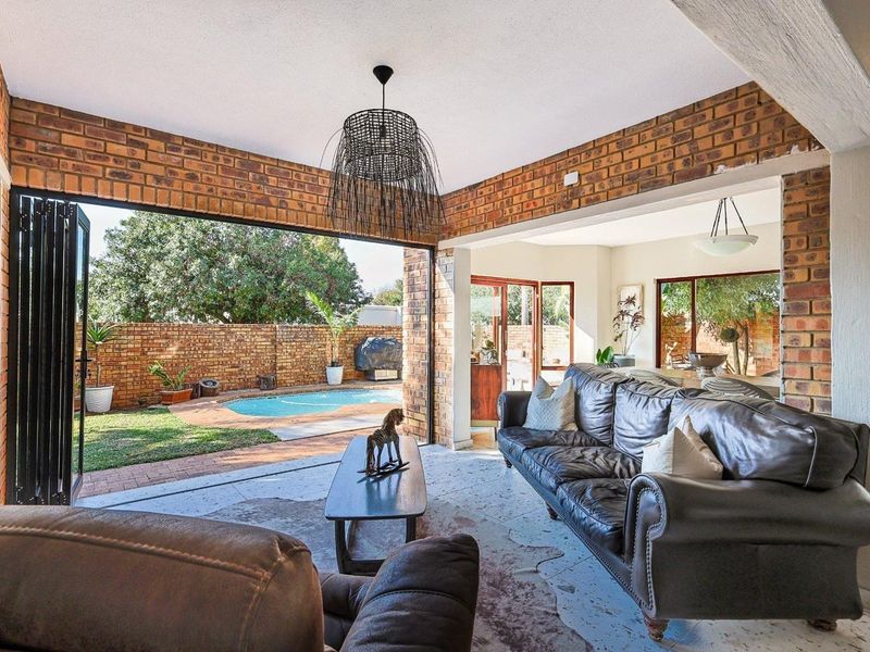 Spacious open-plan living area featuring exposed brick walls and large stacking doors that provide seamless indoor-outdoor flow to the pool and garden area.