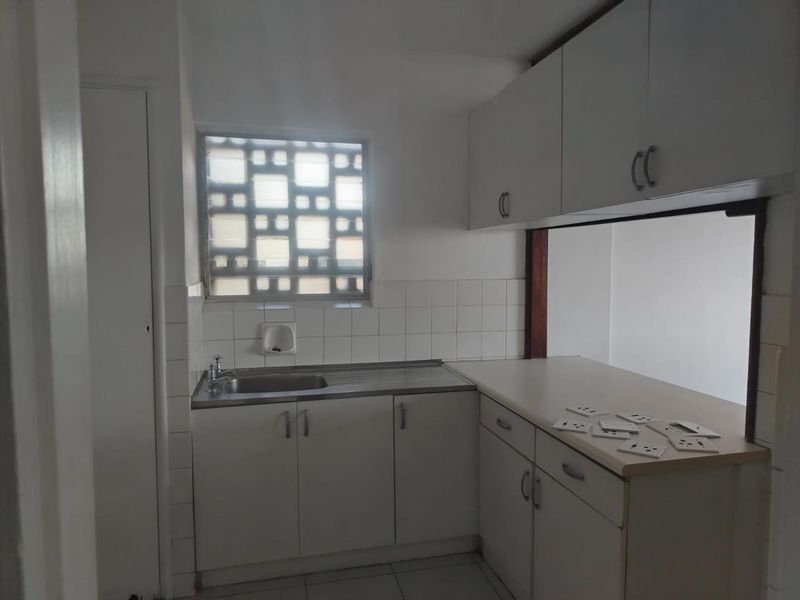 A functional kitchen featuring white built-in cabinetry, a stainless steel sink, tiled backsplash, and a unique decorative breeze block window.
