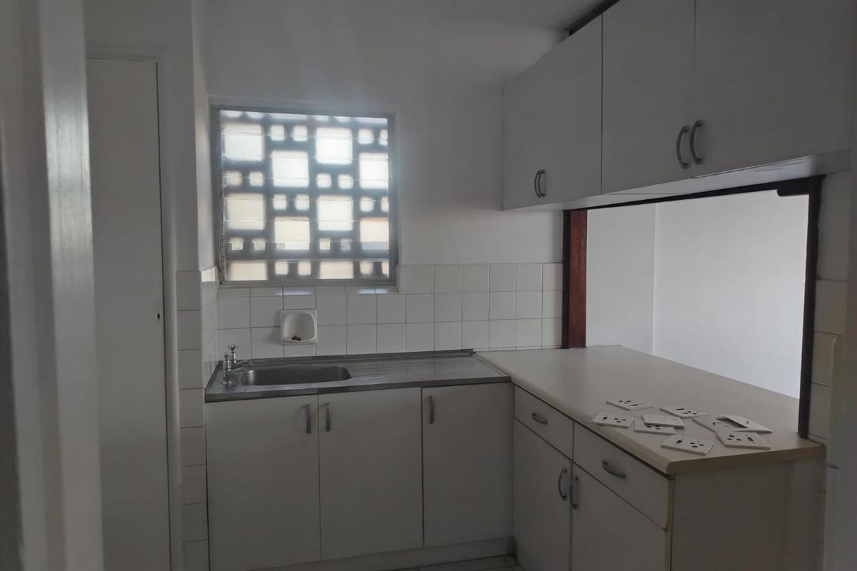 A functional kitchen featuring white built-in cabinetry, a stainless steel sink, tiled backsplash, and a unique decorative breeze block window.