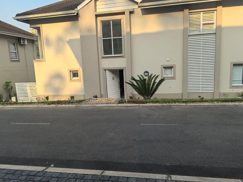 Front elevation of a townhouse featuring a paved entrance, external wall lighting, and white window shutters.