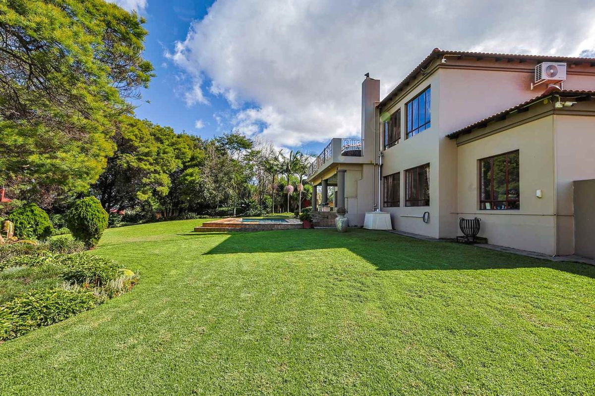 Rear view of the property featuring a spacious lawn, swimming pool, covered patio, and upper-level balcony.