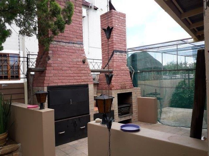 Outdoor entertainment area featuring a dual built-in brick braai and fireplace, tiled flooring, and covered patio space.