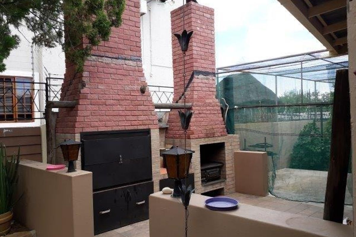 Outdoor entertainment area featuring a dual built-in brick braai and fireplace, tiled flooring, and covered patio space.