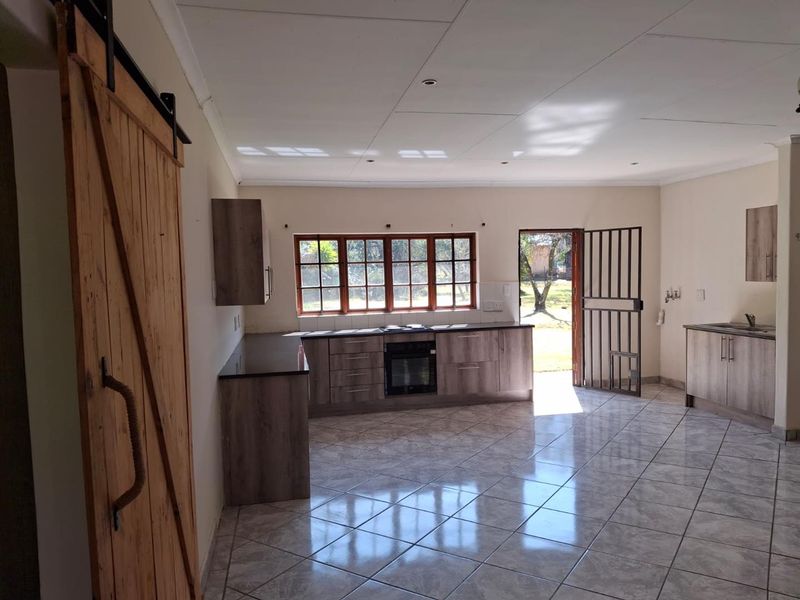 An open-plan kitchen featuring modern wood-look cabinetry, built-in oven and hob, tiled flooring, and direct access to the garden through a security gate.