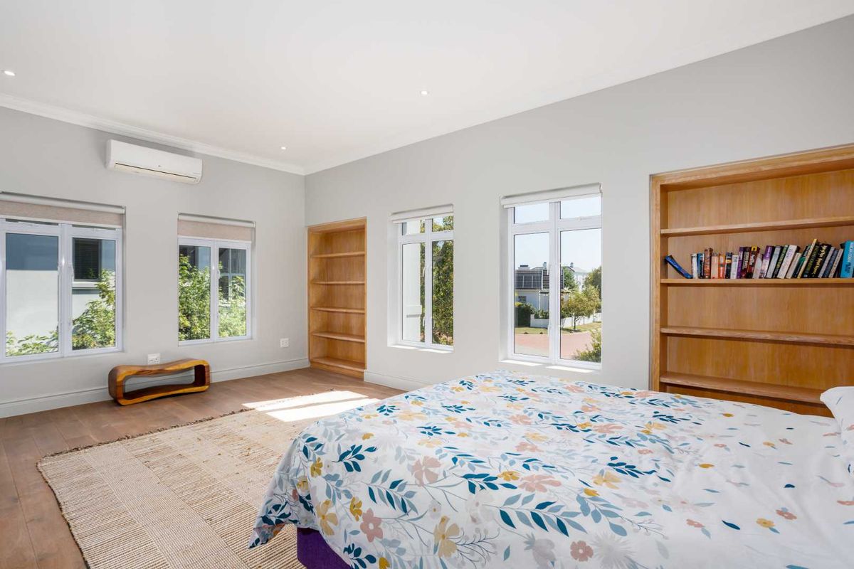 Spacious bedroom featuring timber flooring, built-in wooden shelving units, and a wall-mounted split-system air conditioner with ample natural light.