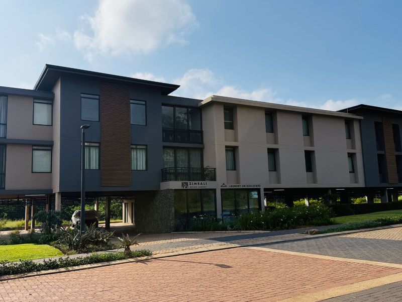 A modern multi-story apartment building featuring a stilt-supported design, stone accents, timber facade detailing, and paved driveway access.