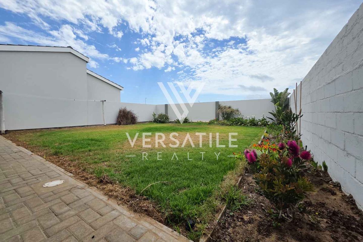 A private rear garden featuring a well-maintained lawn, paved walkway, and perimeter boundary walls with established garden beds.