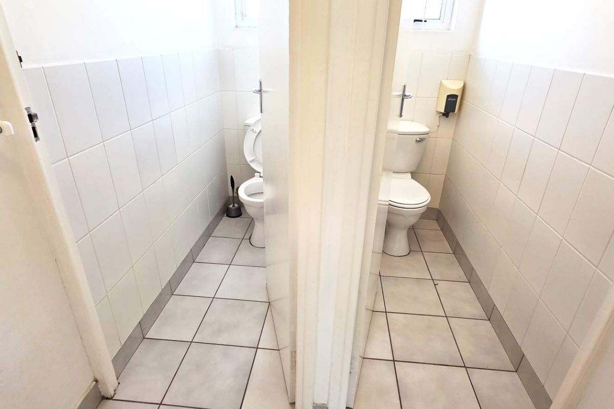 A functional office restroom facility featuring two separate toilet cubicles with tiled walls and floors.