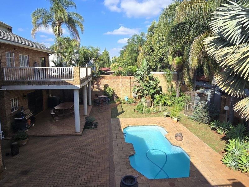 Rear exterior view featuring a brick-faced house with a balcony, covered patio, paved pool area, and established garden.