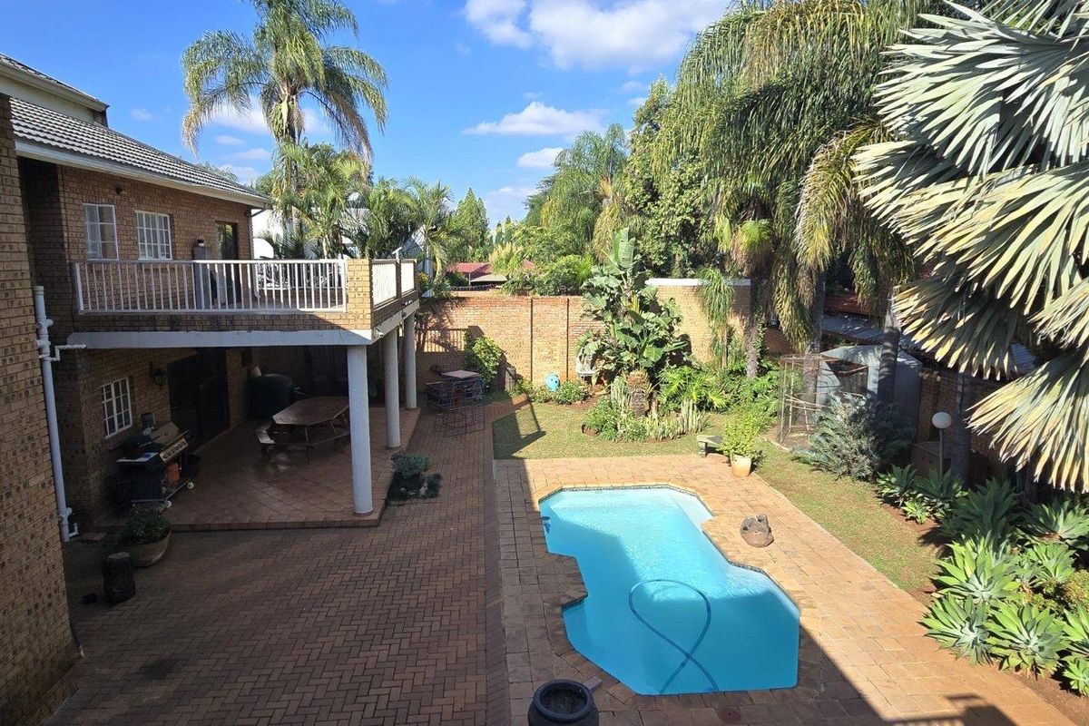 Rear exterior view featuring a brick-faced house with a balcony, covered patio, paved pool area, and established garden.