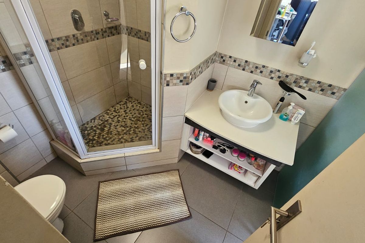 Compact bathroom featuring a corner shower enclosure with mosaic tile accents, a vanity basin, and a wall-mounted toilet.