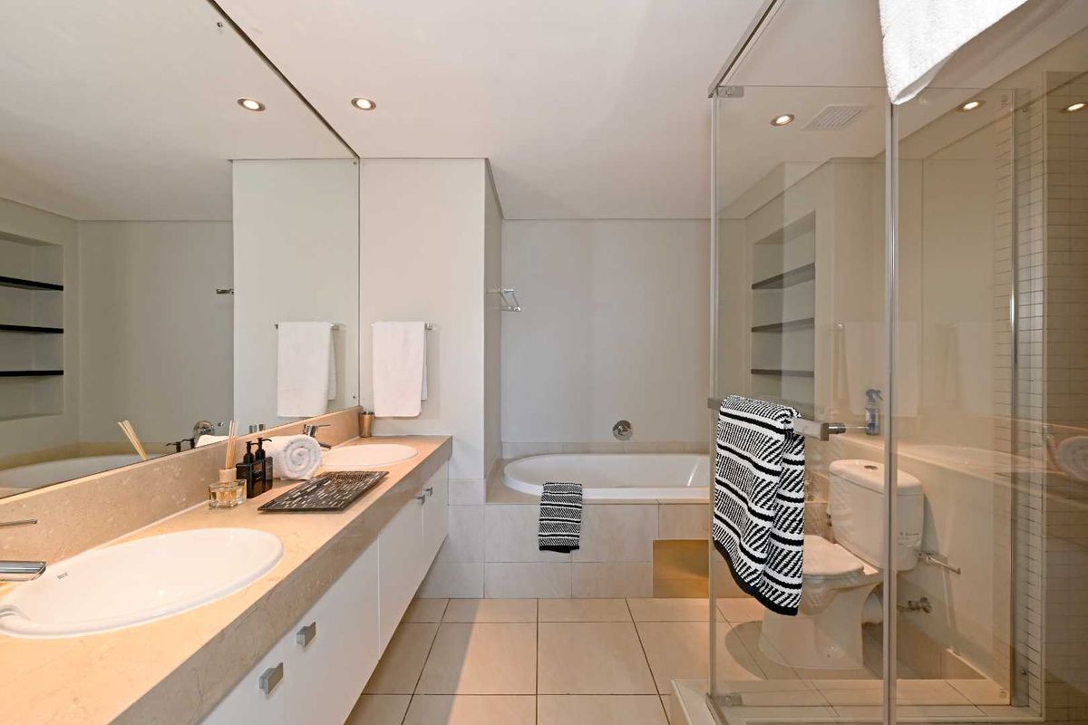 Modern bathroom featuring a double vanity, built-in bathtub, and a separate glass-enclosed shower with neutral tile finishes.