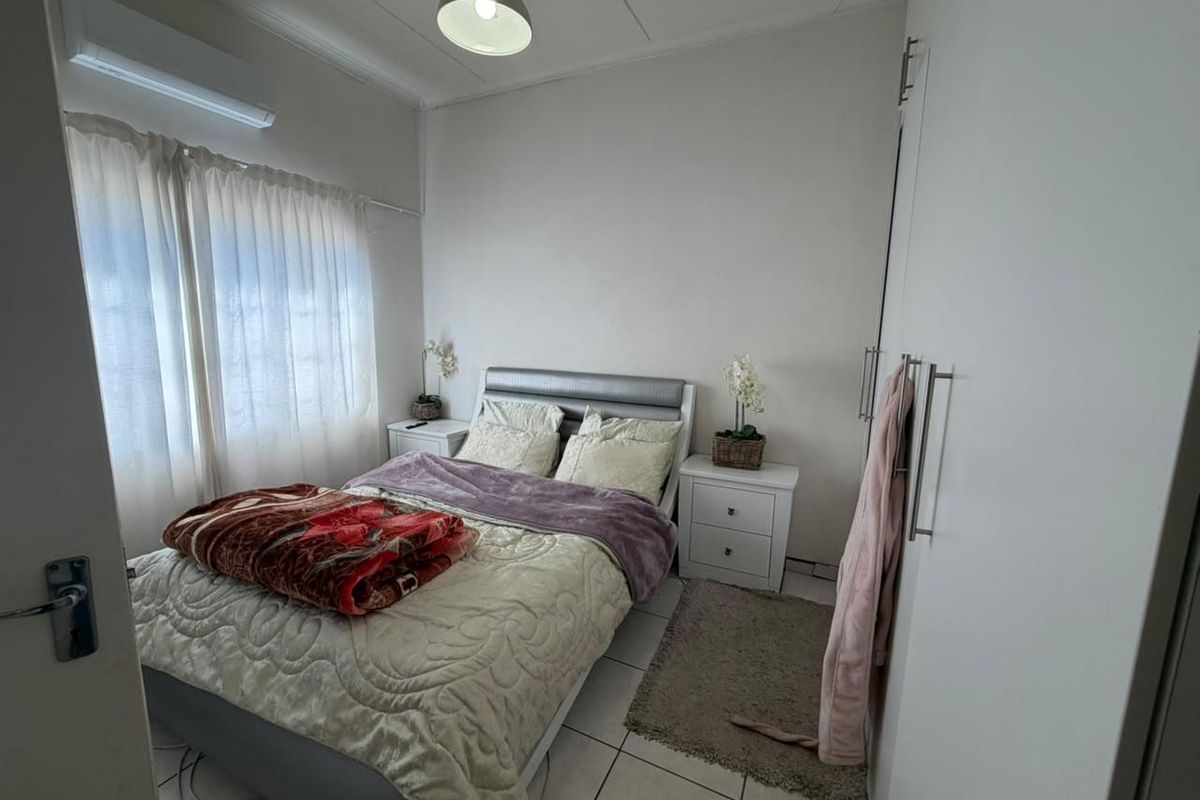 A well-maintained bedroom featuring tiled flooring, built-in cupboards, and a wall-mounted air conditioning unit.