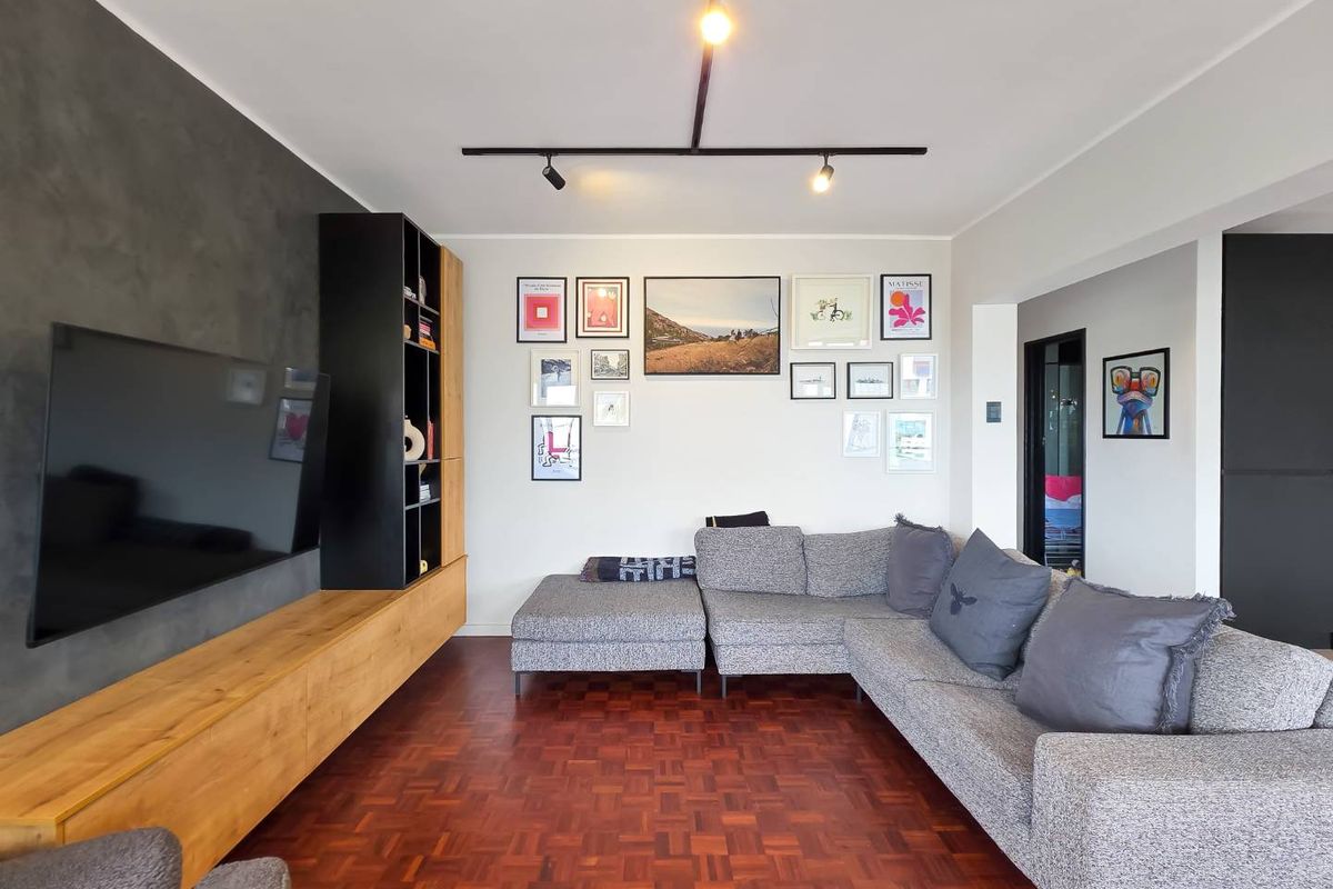 A well-maintained living room featuring rich parquet flooring, modern track lighting, and a custom built-in media console with integrated shelving.