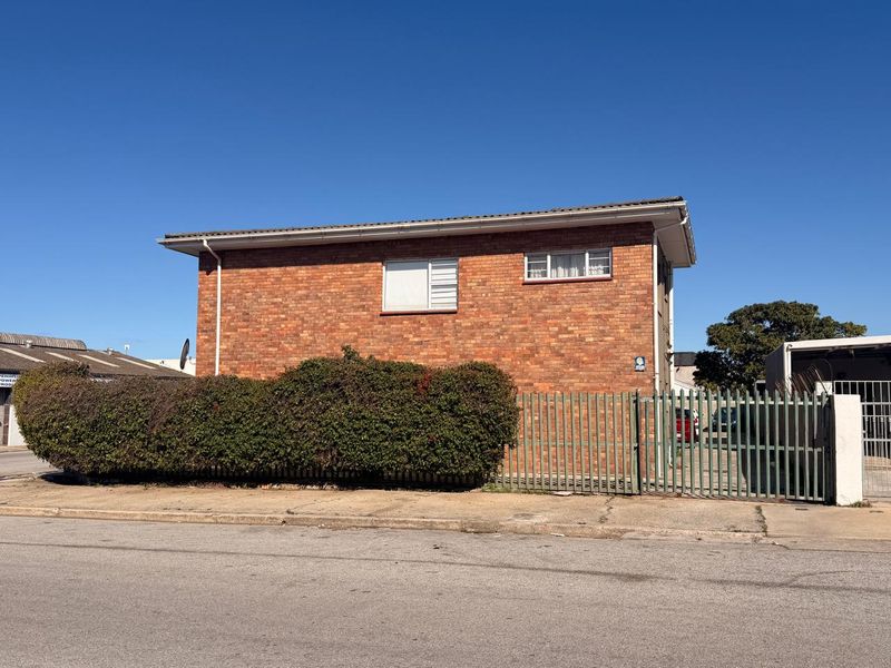 Street-facing view of a brick apartment building featuring metal security fencing and established perimeter hedging.