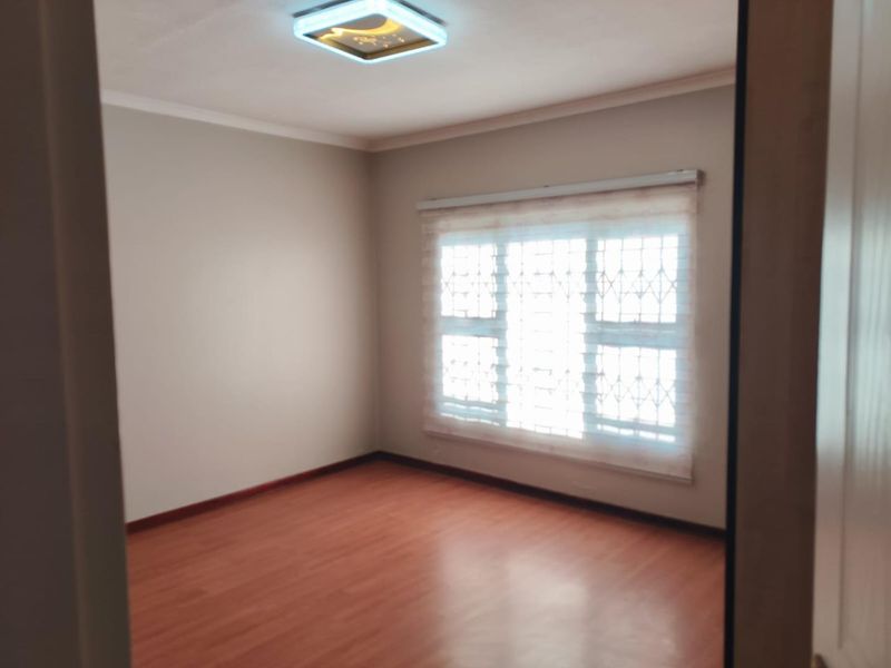 A clean, empty bedroom featuring laminate flooring, a security gate on the window, and a modern ceiling light fixture.