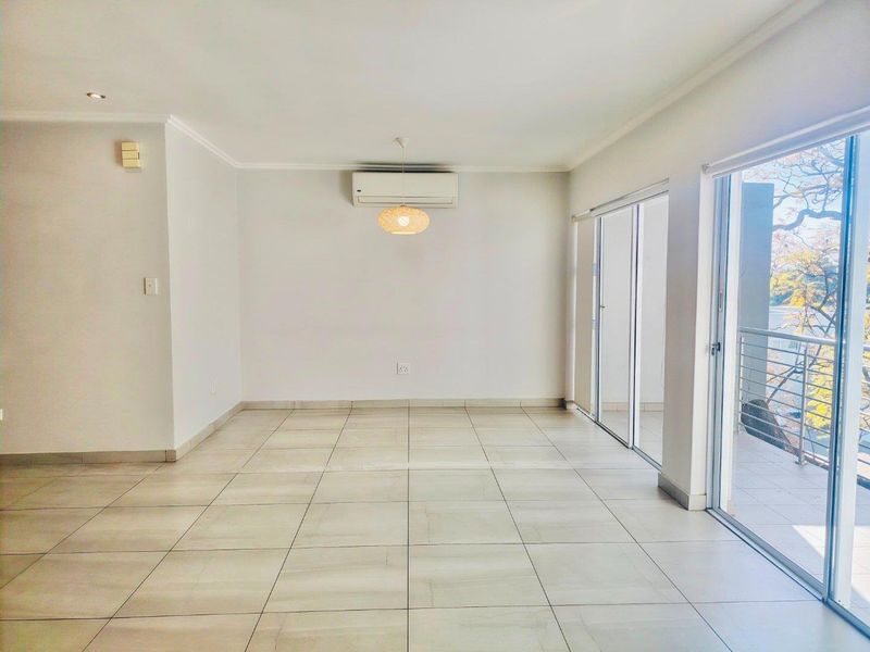 A bright, empty living area featuring neutral tiled flooring, a wall-mounted air conditioning unit, and large sliding glass doors leading to a balcony.