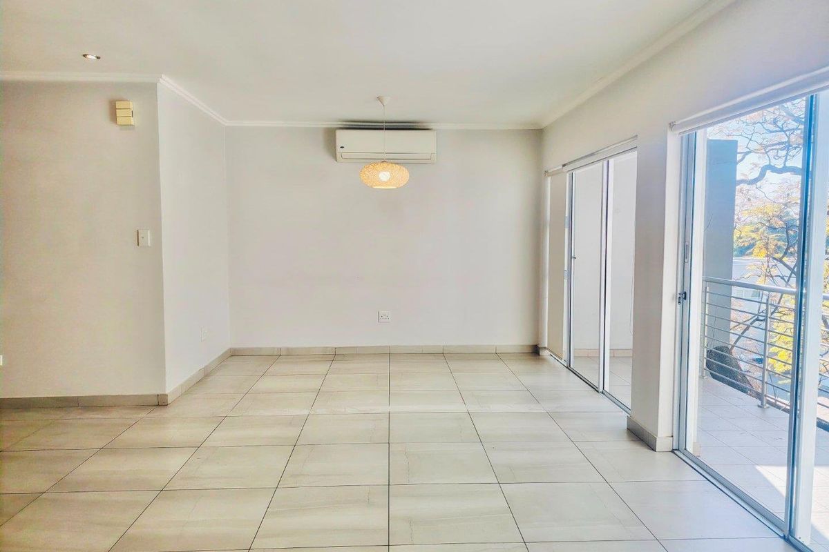 A bright, empty living area featuring neutral tiled flooring, a wall-mounted air conditioning unit, and large sliding glass doors leading to a balcony.