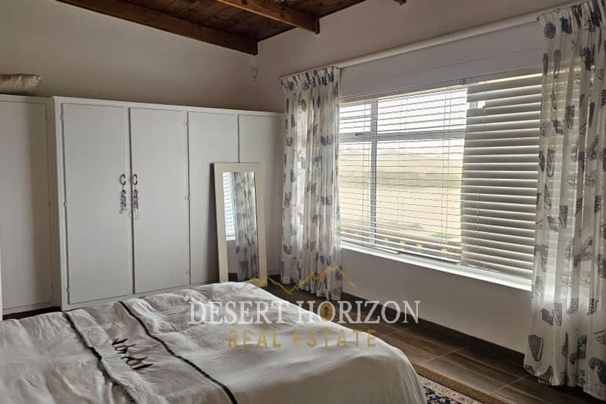A bedroom featuring built-in wardrobes, exposed timber ceiling beams, and large windows with blinds, offering a view of the surrounding landscape.