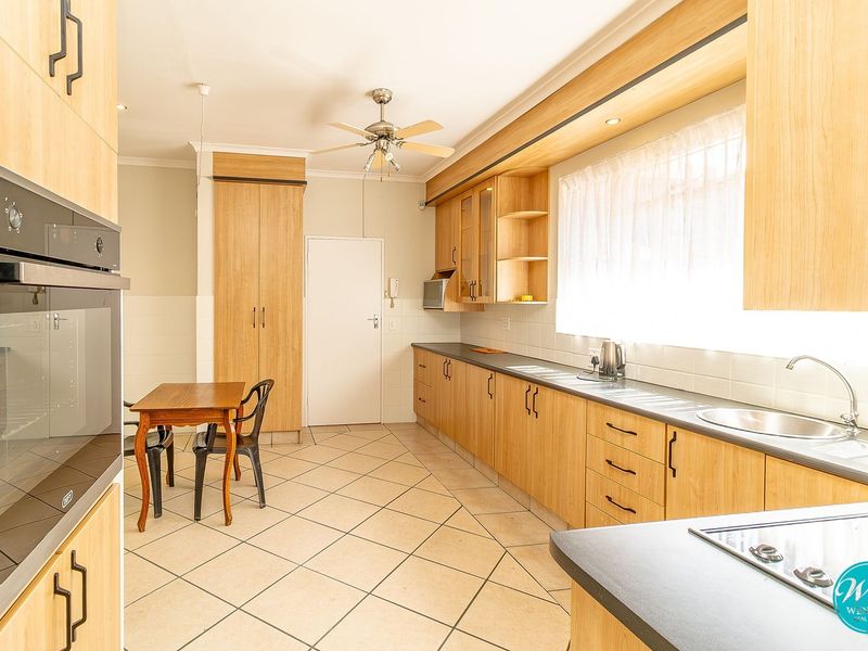 A functional kitchen featuring light wood-finish cabinetry, tiled flooring, a built-in oven, and a hob, offering ample storage and workspace.