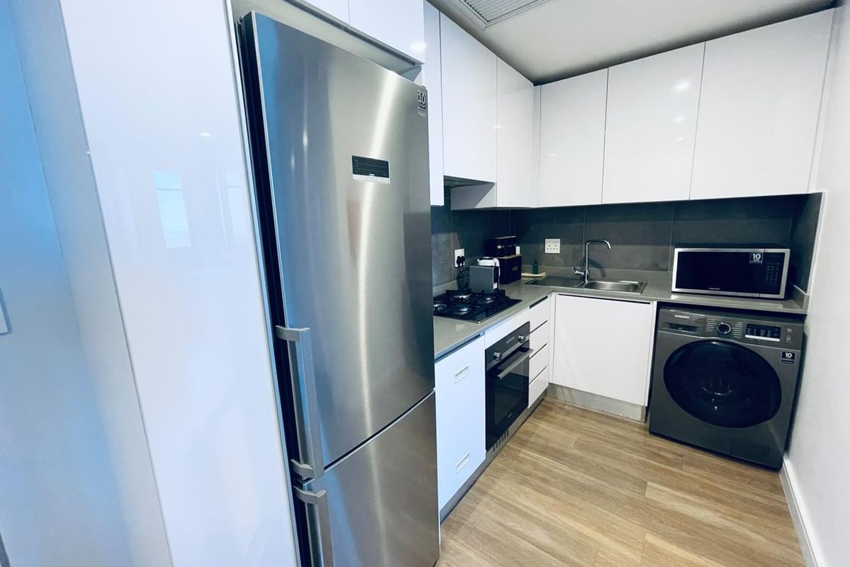 Modern compact kitchen featuring high-gloss white cabinetry, stone countertops, integrated appliances, and durable laminate flooring.