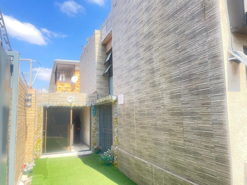 Rear exterior view of the guest house featuring a stone-clad facade, artificial turf area, and a sliding glass door entrance.