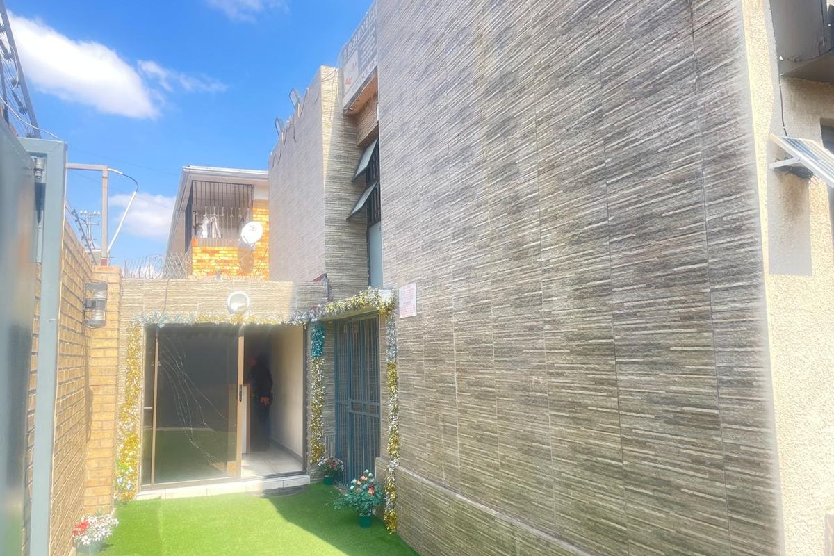 Rear exterior view of the guest house featuring a stone-clad facade, artificial turf area, and a sliding glass door entrance.
