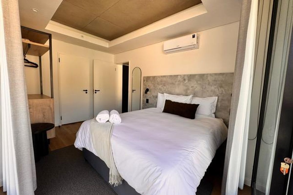 Modern bedroom featuring a recessed ceiling, built-in wardrobe, wall-mounted air conditioning unit, and a concrete-look headboard panel.
